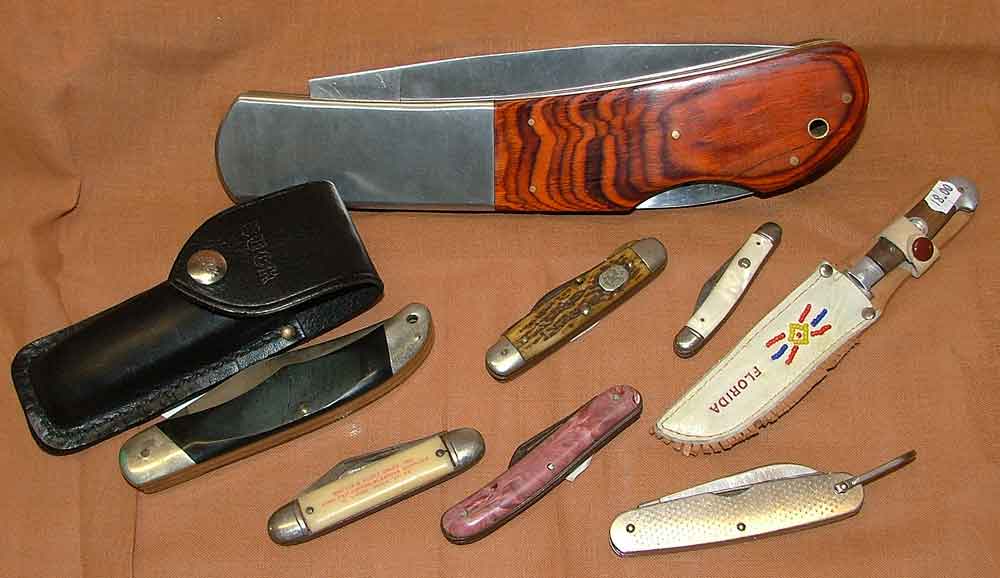 A variety of Knives available at Bahoukas in Havre de Grace - Buck Knife w/black case, Boy Scout Knife 1950s, Imperial Pocket knife, a Florida souvenir knife with compass on handle, Johnston Mfg peralized handle knife with 2" blade, and a US Military knife by Camillus 1977